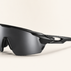 Futuristic black sporty wraparound sunglasses with a curved smoke lens on a warm gray background