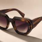 Geometric tortoiseshell acetate sunglasses with gradient lenses resting on a neutral, textured surface.