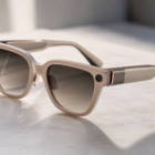 Beige oversized sunglasses with dark gradient lenses resting on a light marble surface, showing metallic hinges.