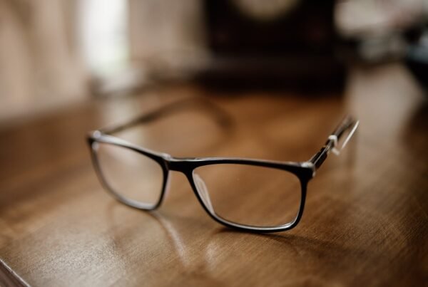 Close-up of black rectangular eyeglasses resting on a wooden desk with a blurred background