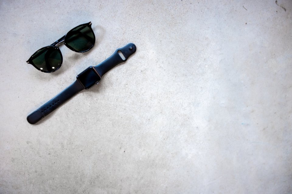 Core carryover eyewear assortment: unbranded black sunglasses with everyday lifestyle flat-lay on neutral surface, no brand marks