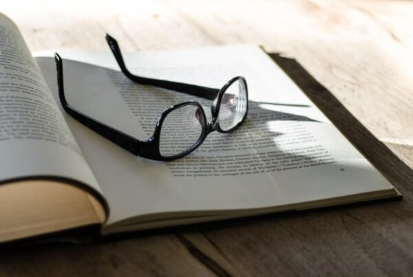 Glasses resting on open book pages on a wooden table in sunlight.