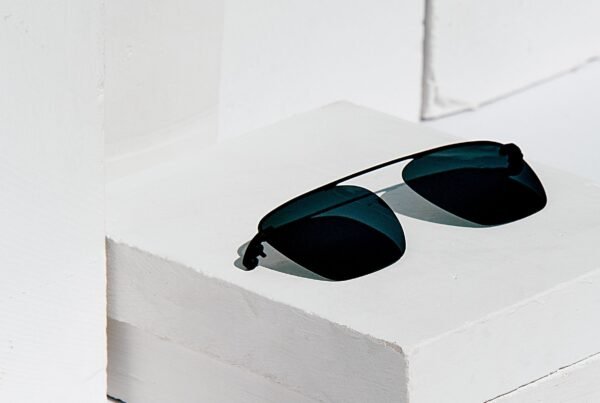Black sunglasses resting on a white stair step with bright, minimal background shadows nearby