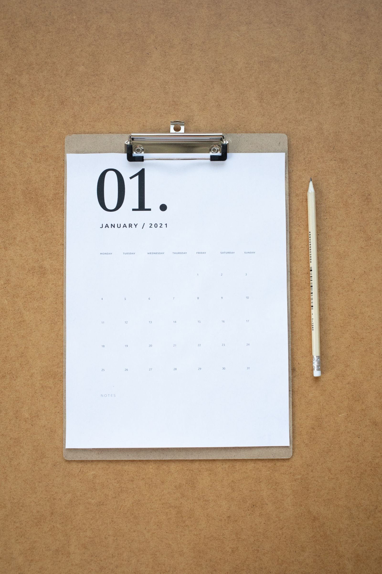 Eyewear replenishment cadence: blank calendar clipboard and pencil for qualitative reorder window and mid-season replenish planning, no brand marks