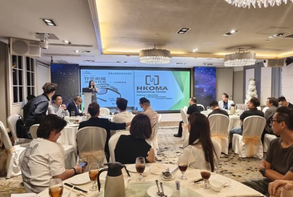 Networking dinner in a banquet hall; presenter at podium with large HKOMA screen, guests seated at round tables.