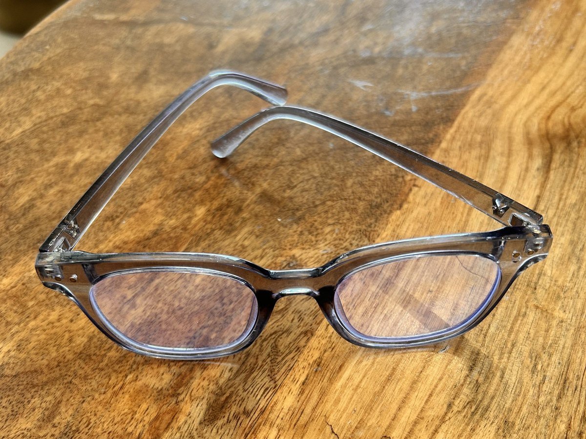 Unbranded smoke-grey crystal optical frame on a wooden table, an example of injection frame finishes