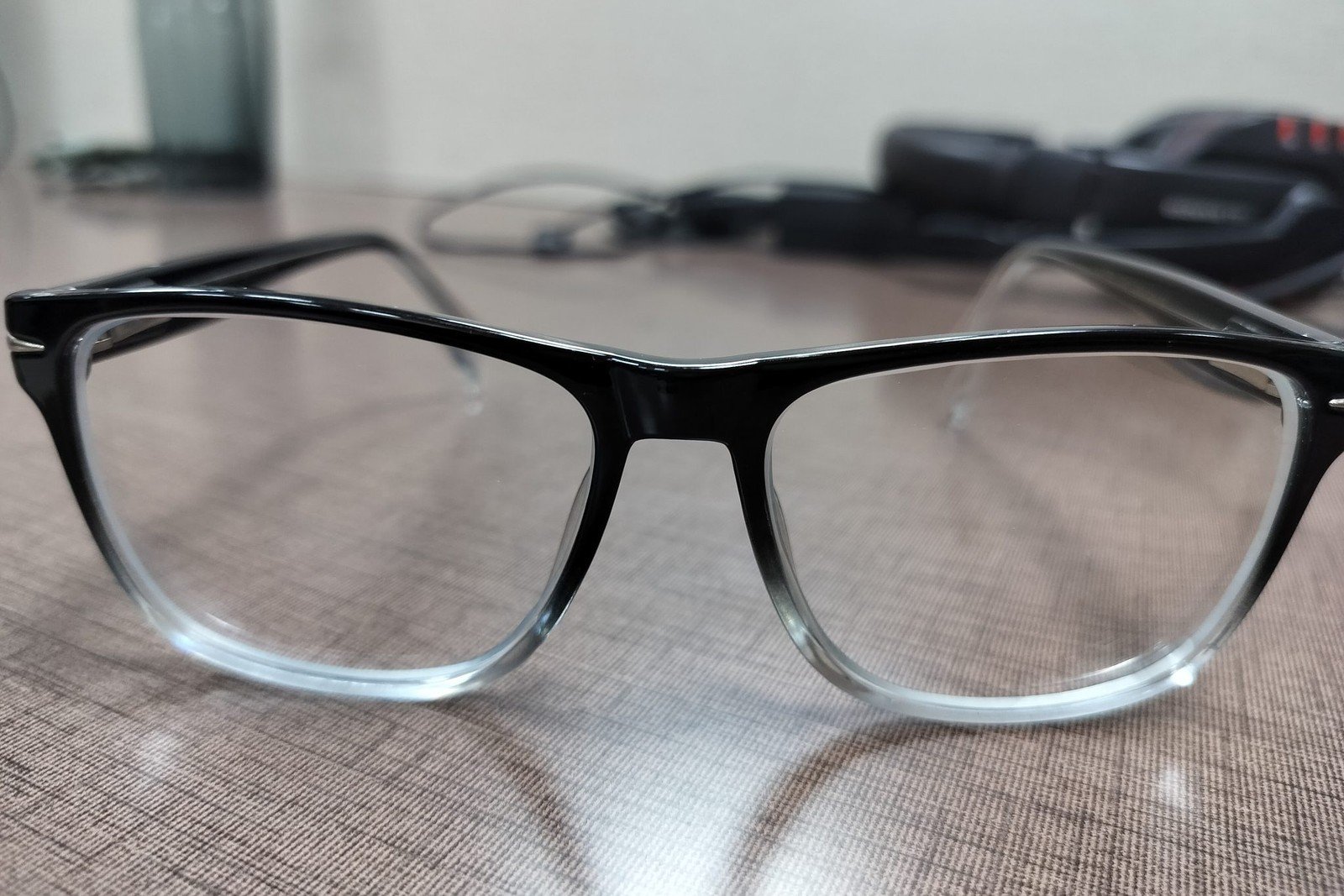 Unbranded black-to-clear optical frames on a desk, an open-ear audio glasses manufacturer style built as fashion eyewear